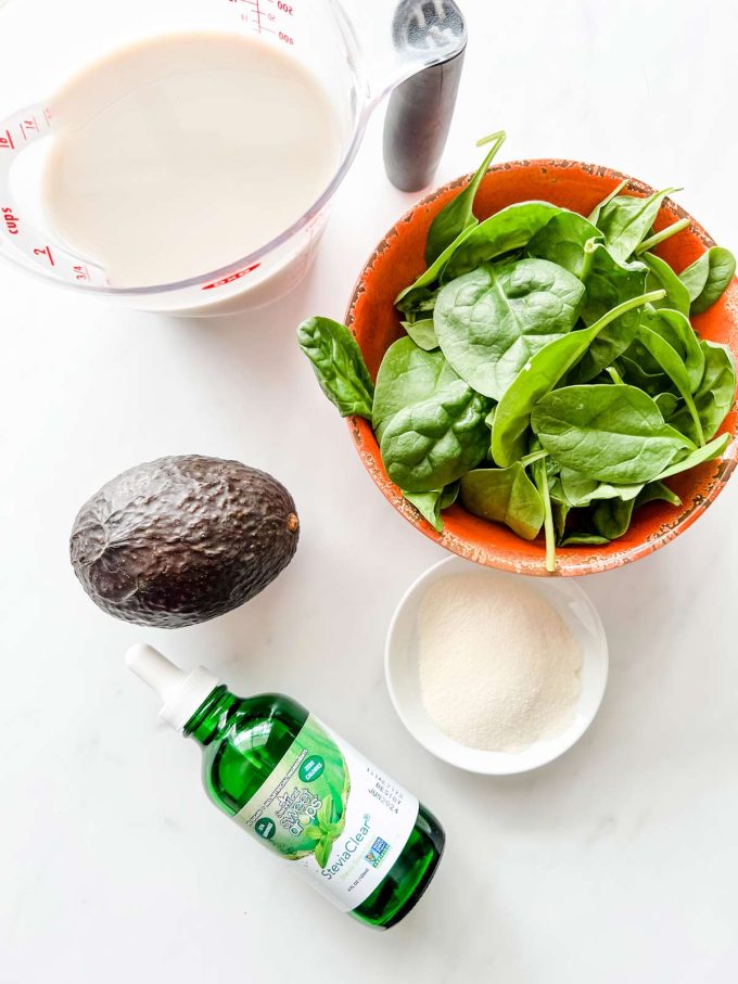 Overhead photo of almond milk, spinach, protein powder, avocado, and stevia.