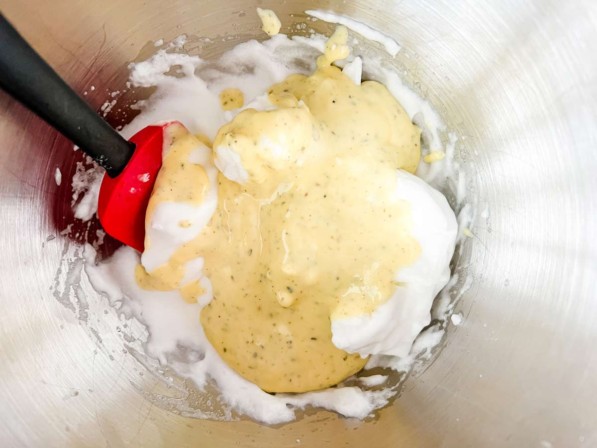 Horizontal image of whipped egg whites being stirred with egg yolks, cream cheese, and seasonings.