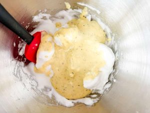 Egg yolks, cream cheese, and seasonings being stirred into beaten egg whites.