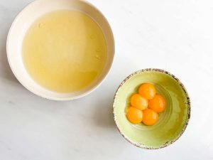 A bowl of egg whites next to a bowl of egg yolks.