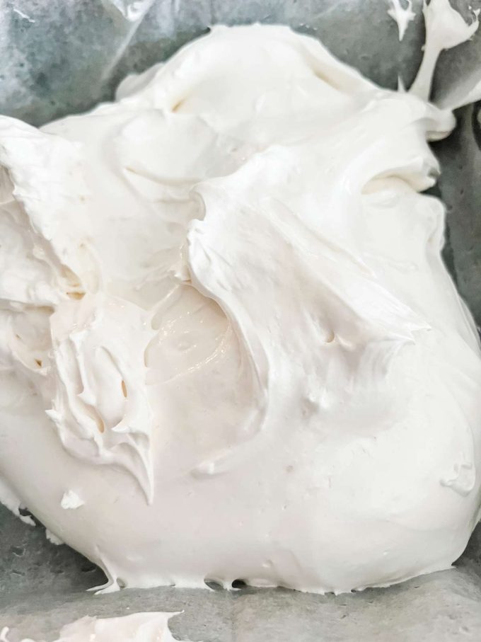 Whipped keto marshmallows being added to a parchment lined dish.