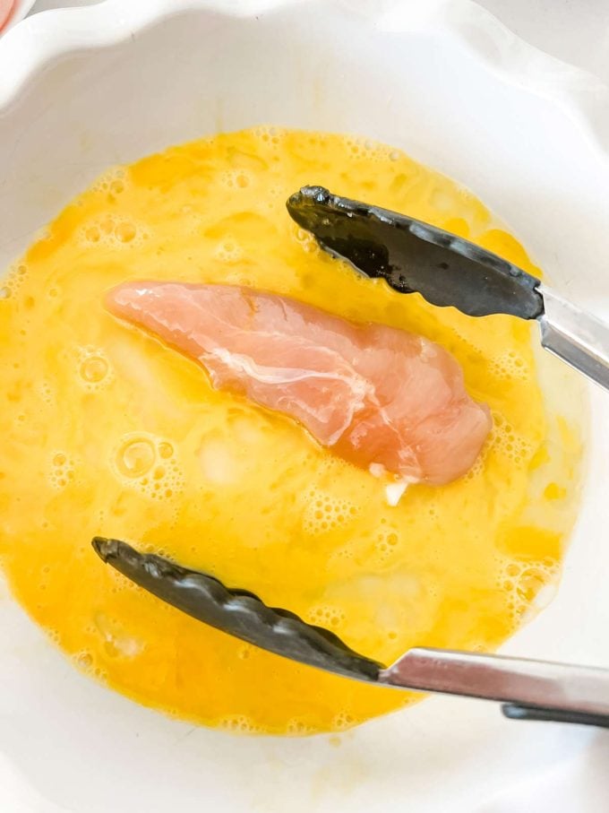 A chicken tender being dipped in eggs.