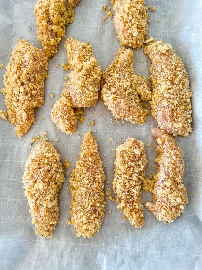 Breaded chicken tenders on a parchment lined baking sheet.