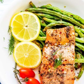 Overhead photo of keto air fryer salmon on a white plate with green beans, cherry tomato, and lemon slices.