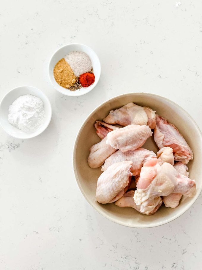 Overhead photo of a bowl of chicken flats and drumettes, seasonings, and baking powder.
