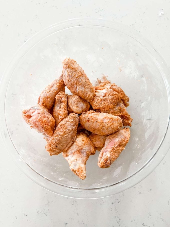 Chicken wings that have been coated with baking powder, garlic powder, salt, smoked paprika and black pepper in a glass bowl.