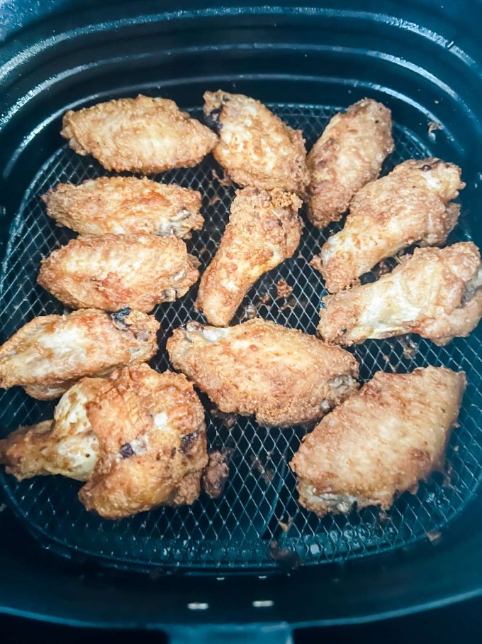 Chicken wings halfway cooked in an air fryer basket.