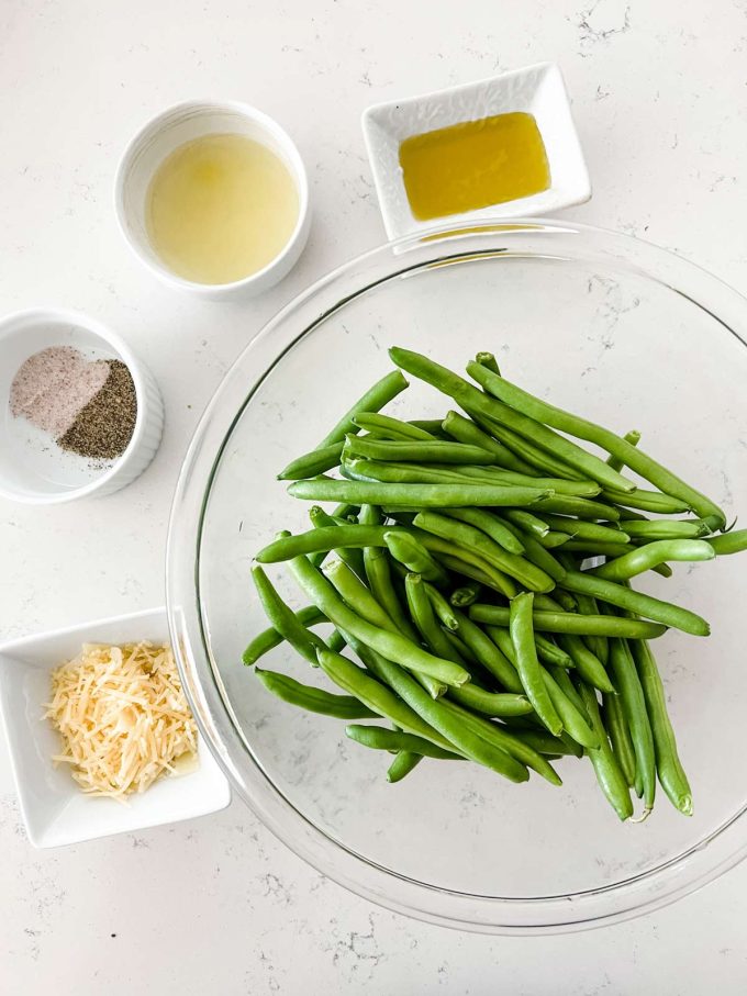 Over head photo of a glass bowl of green beans, oil, lemon juice, parmesan, and seasonings.
