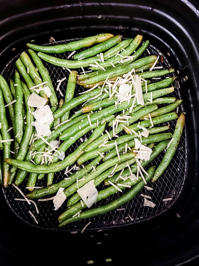 Photo of green beans in an air fryer with parmesan cheese on top of them.