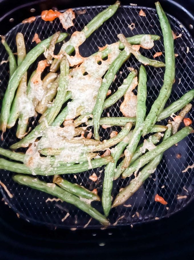Photo of green beans with melted parmesan on top in an air fryer basket.