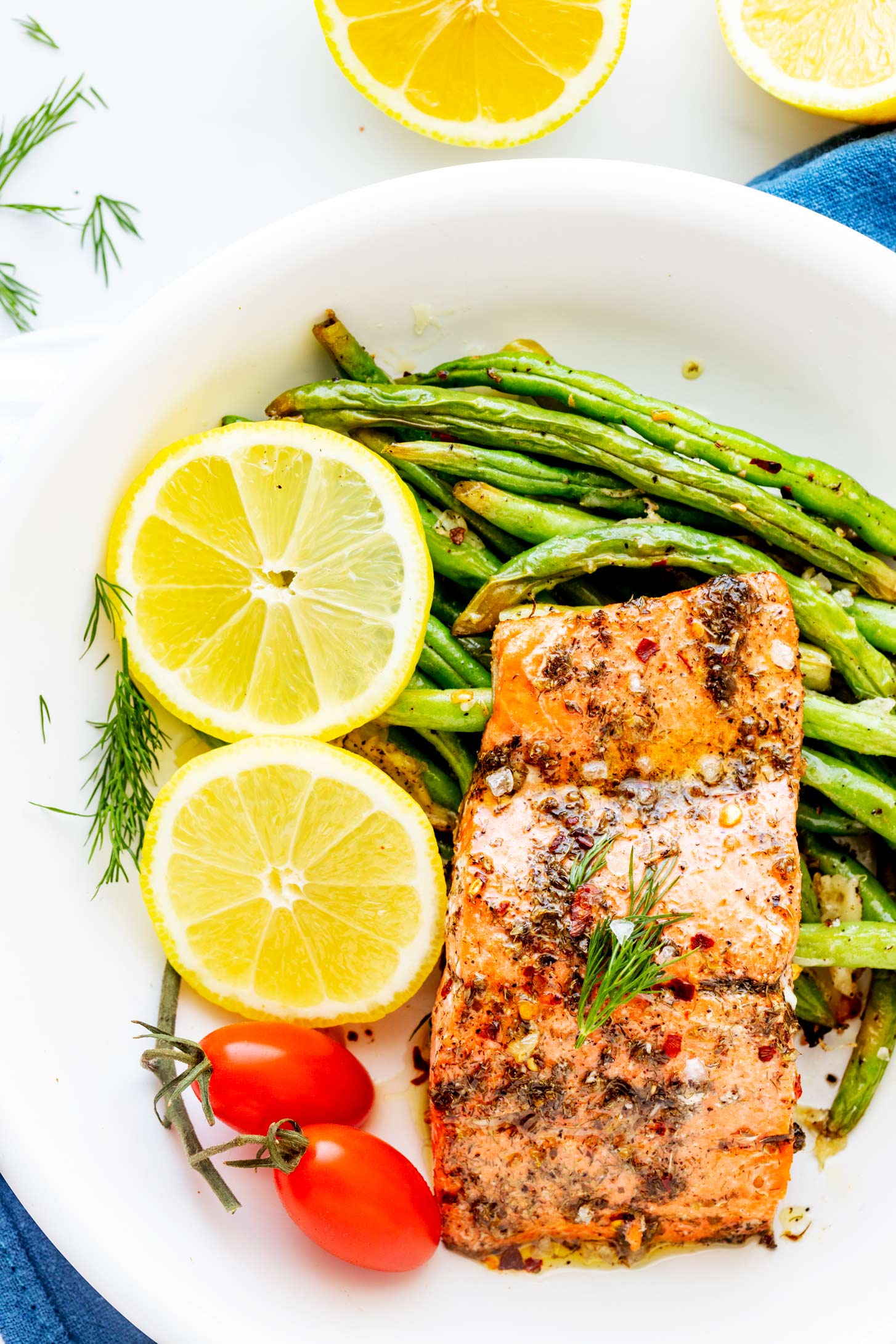 Overhead photo of keto air fryer salmon on a white plate with green beans, cherry tomato, and lemon slices.