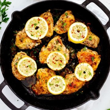 Overhead photo of a cast iron skillet with handles with lemon pepper chicken thighs.