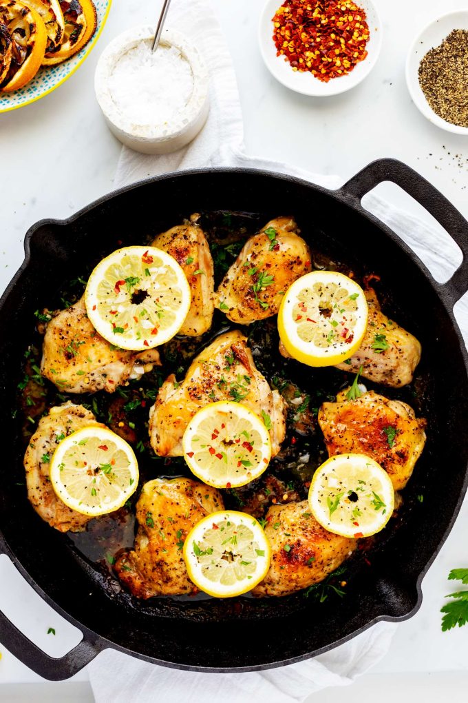 Photo of a cast iron skillet with cooked lemon pepper chicken thighs garnished with parsley and lemon sliced.