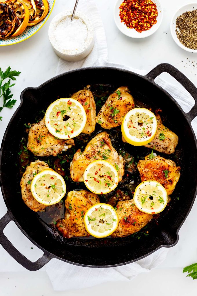 Overhead photo of a skillet with lemon pepper chicken thighs in it covered with sliced lemons.