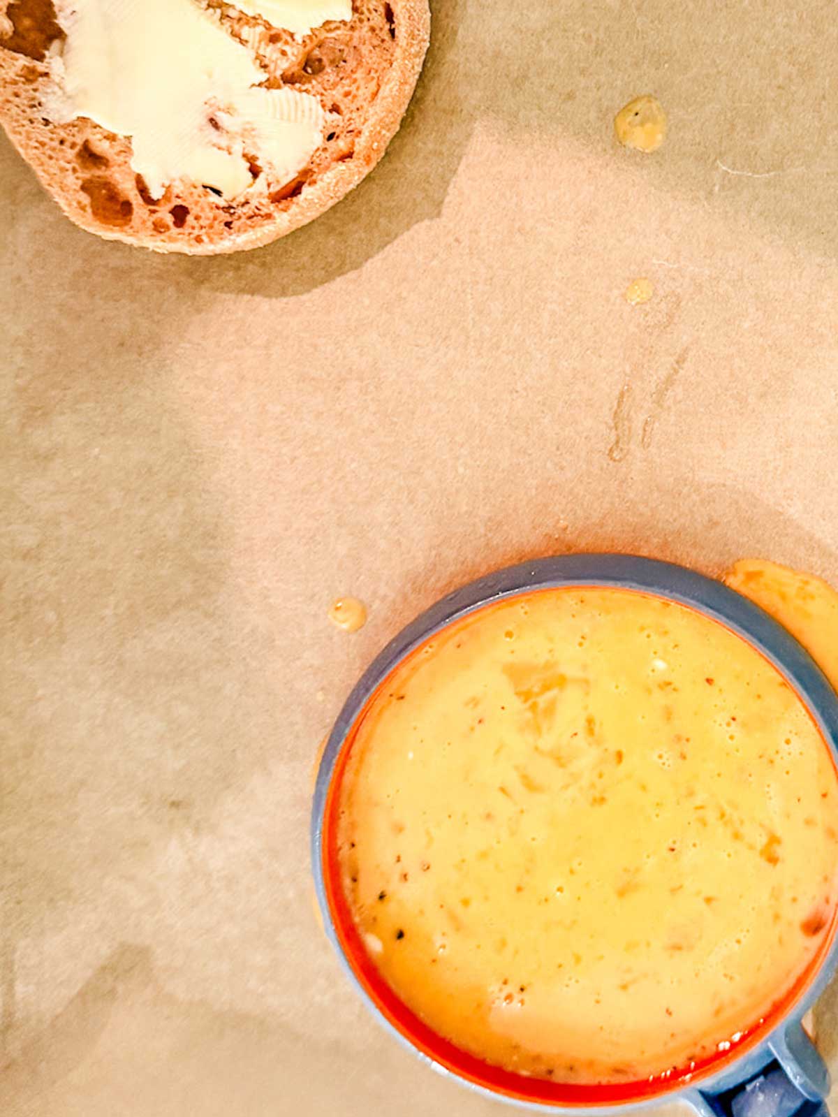 An egg in an egg ring on a sheet pan with a buttered English muffin sititng next to it.
