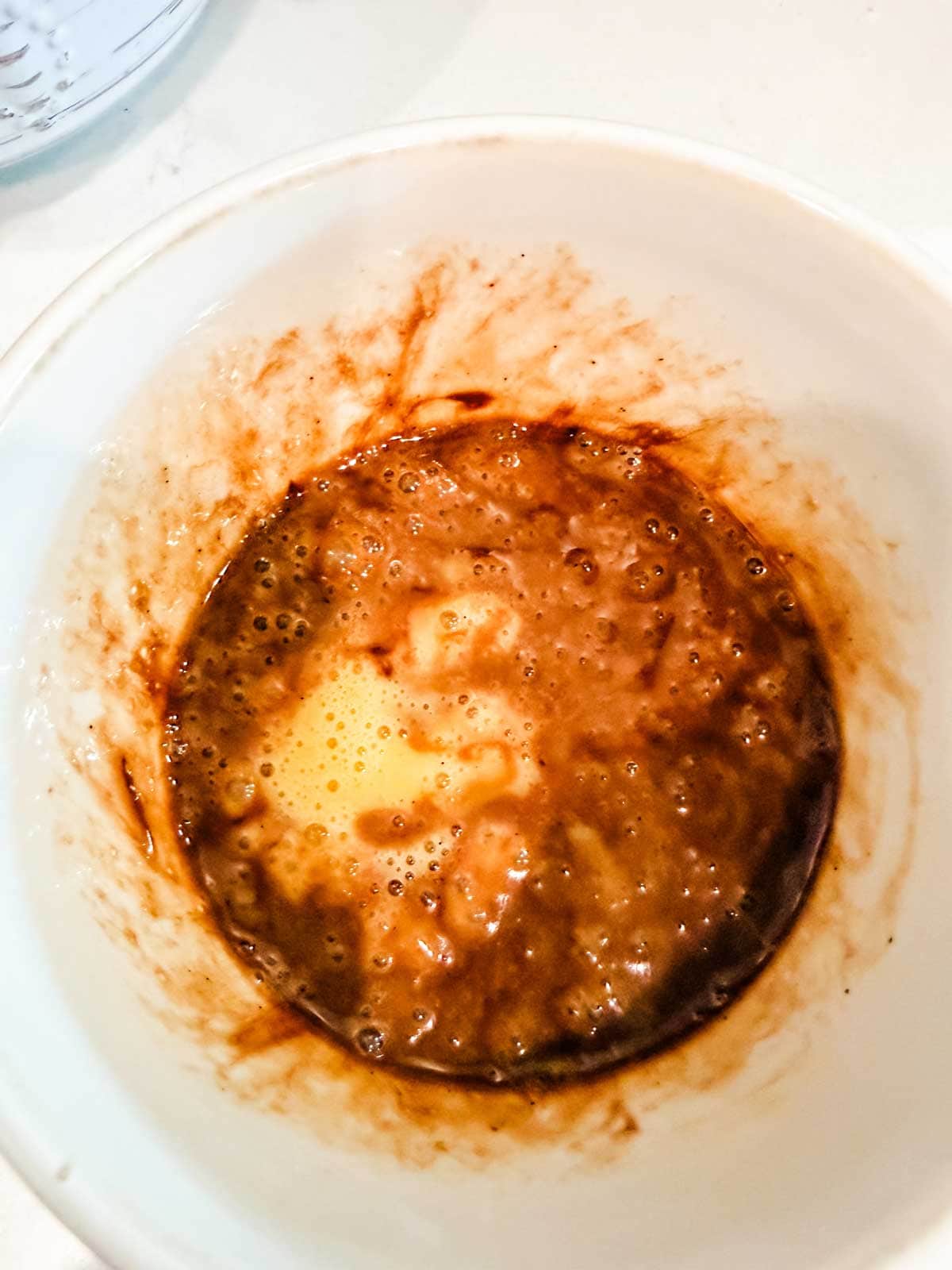 A white mug with chocolate chips and butter on a light-colored surface.