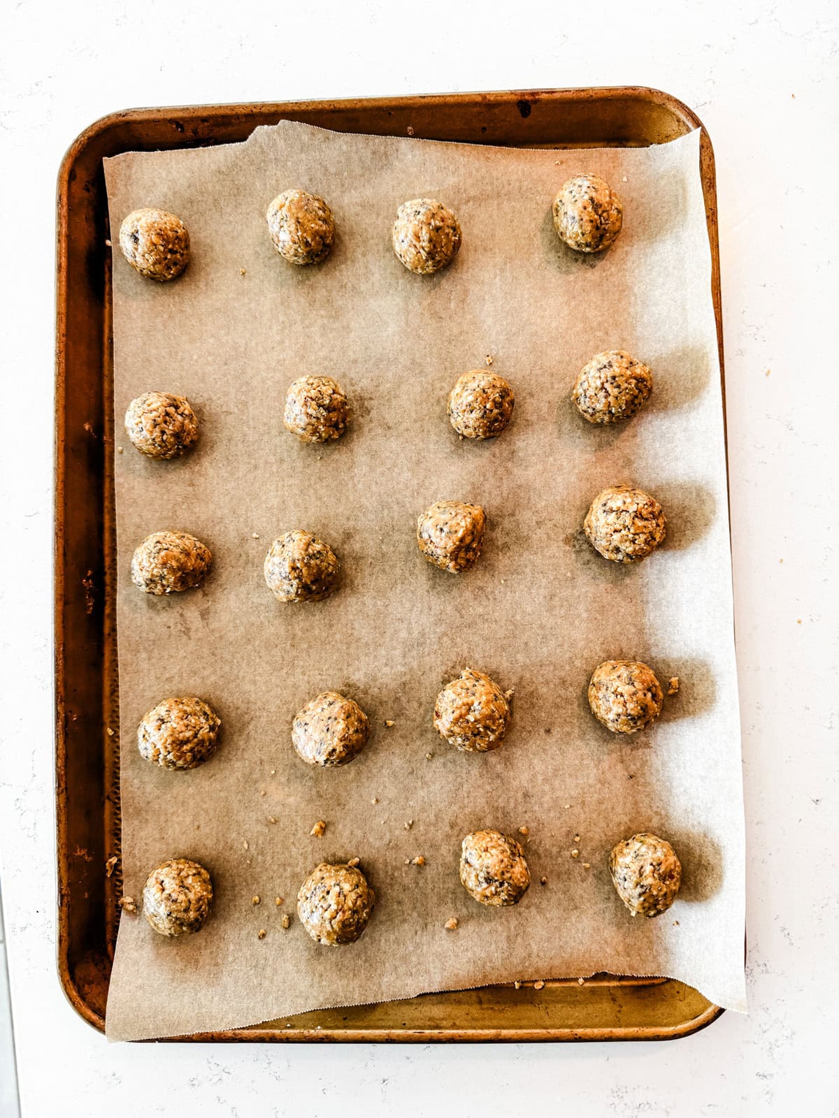 A baking tray lined with parchment paper holds twenty evenly spaced, almond butter bites.