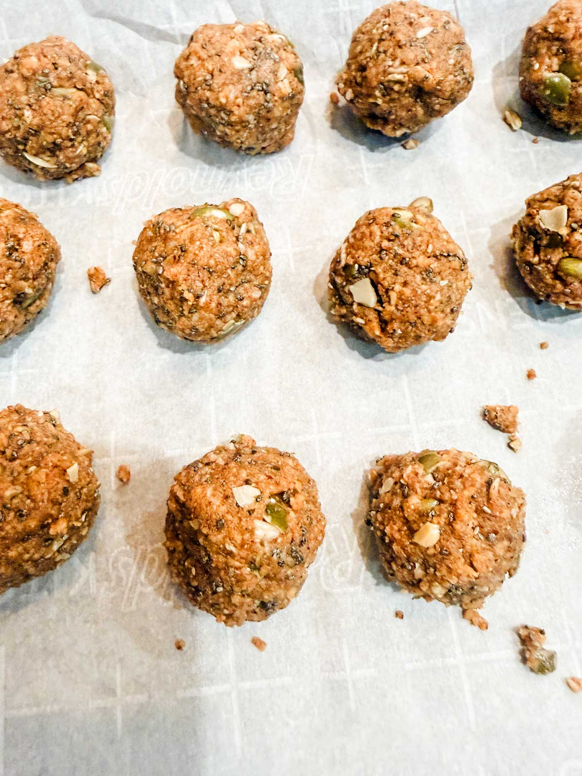 Twelve unbaked energy bites made with coconut, seeds, and nuts are arranged on a sheet of parchment paper.