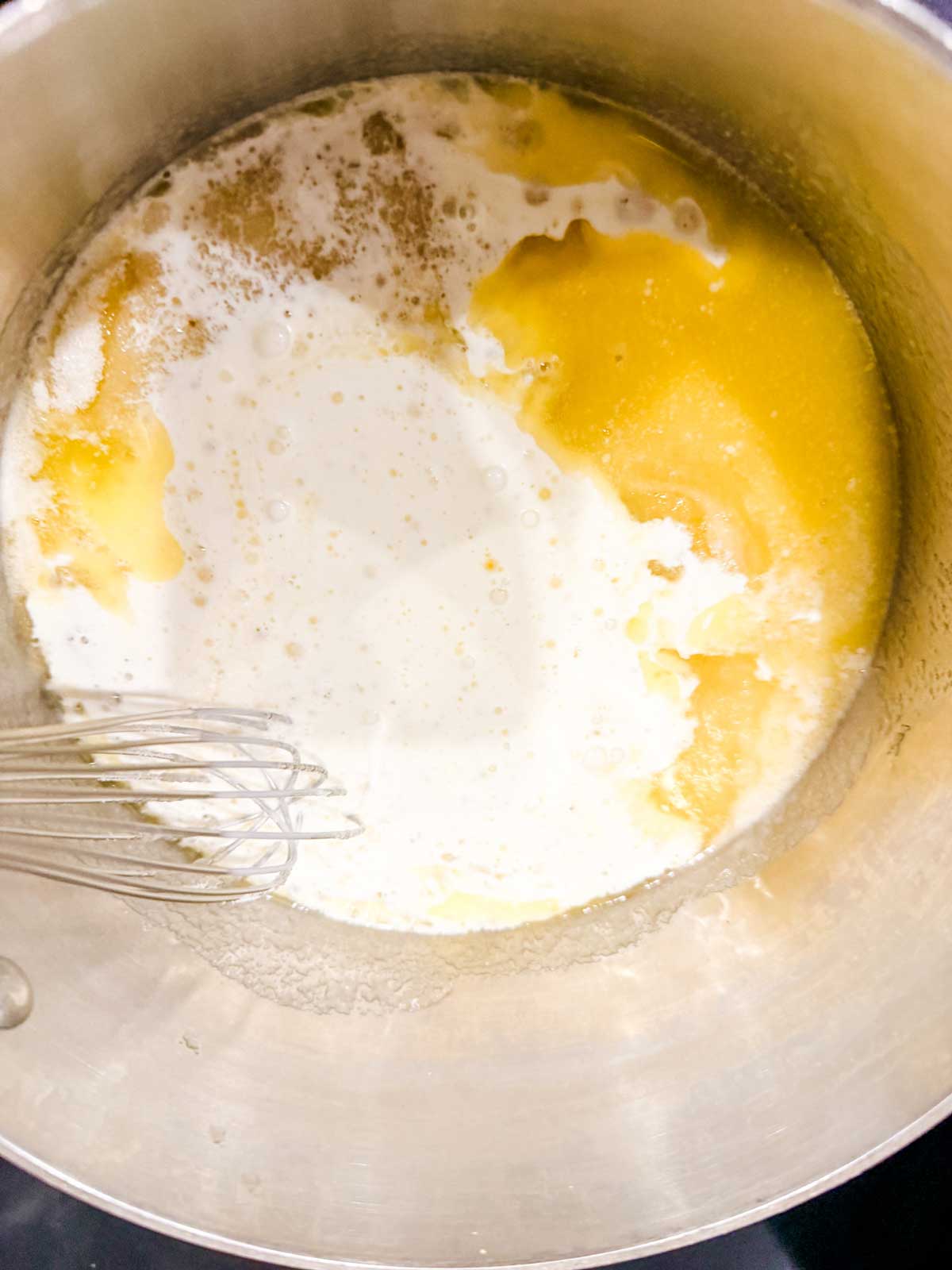 A saucepan with melted butter and cream being whisked together, starting to blend.
