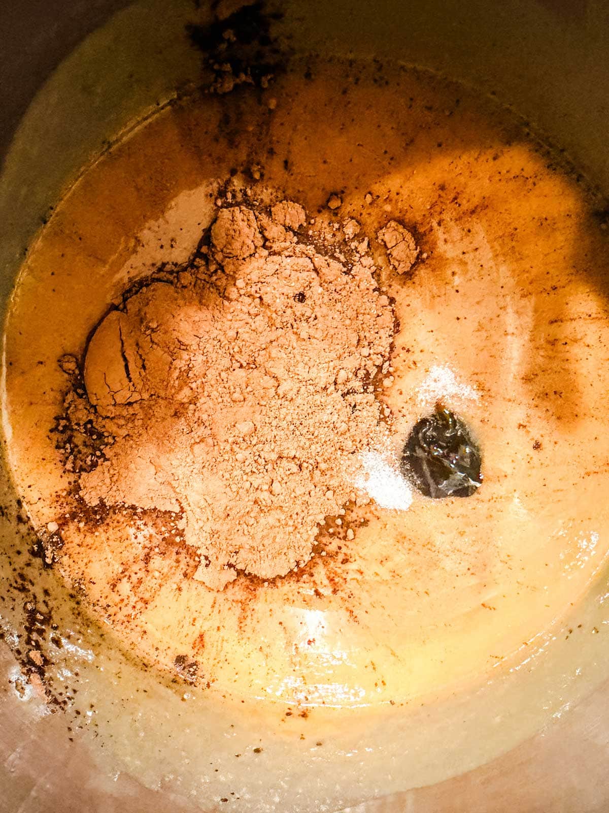 A close-up of a sauce pan with cocoa powder, a small bit of salt, and vanilla on top of a liquid mixture.