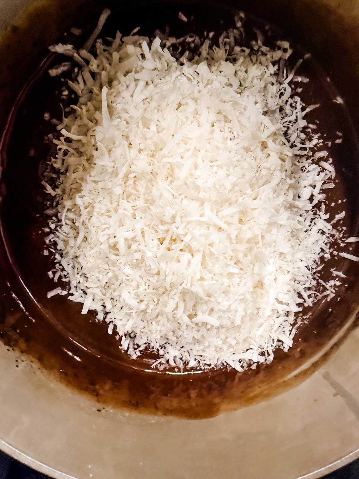Shredded coconut sits on top of a mixture of melted chocolate in a mixing bowl, ready to be combined.