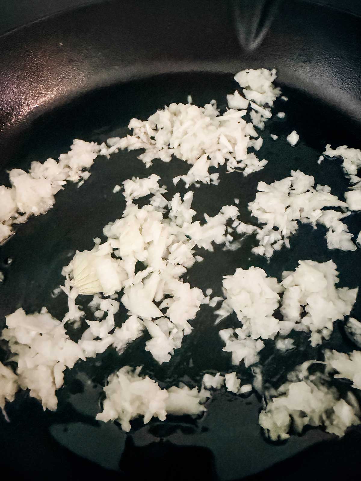 Chopped onion sautéing in oil in a black frying pan.