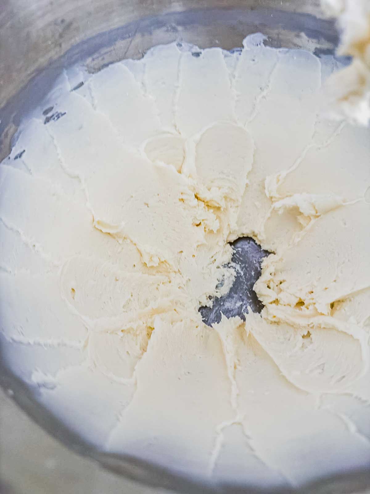 Close-up of smooth, creamy white mixture in a mixing bowl, with a spatula having scraped circular lines outward from the center, revealing the bottom of the bowl.