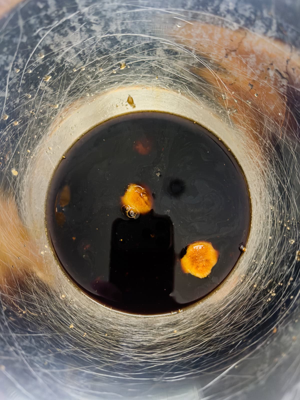 A close-up view of a scratched transparent cup containing a dark liquid with two cloves of garlic added.