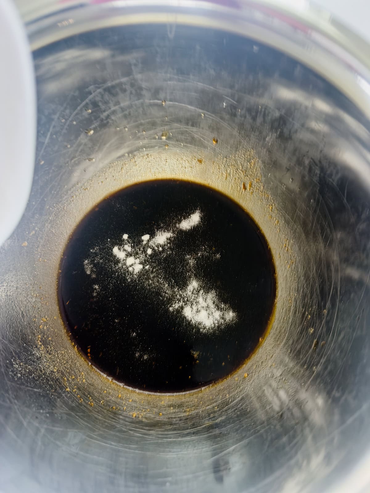 A metal mixing bowl with a small amount of dark liquid and xanthan gum.