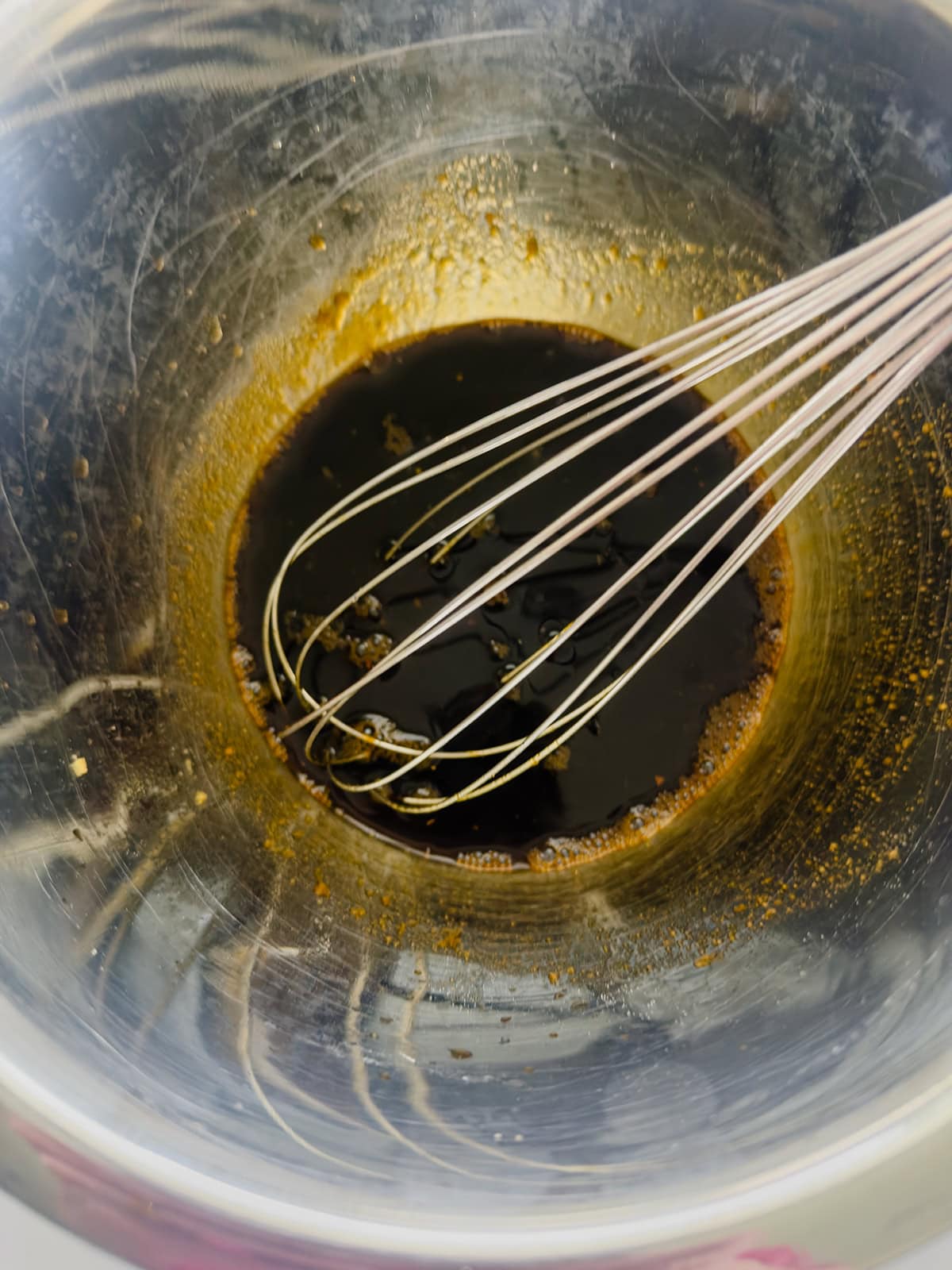 A metal whisk rests in a stainless steel bowl containing keto stir fry sauce.