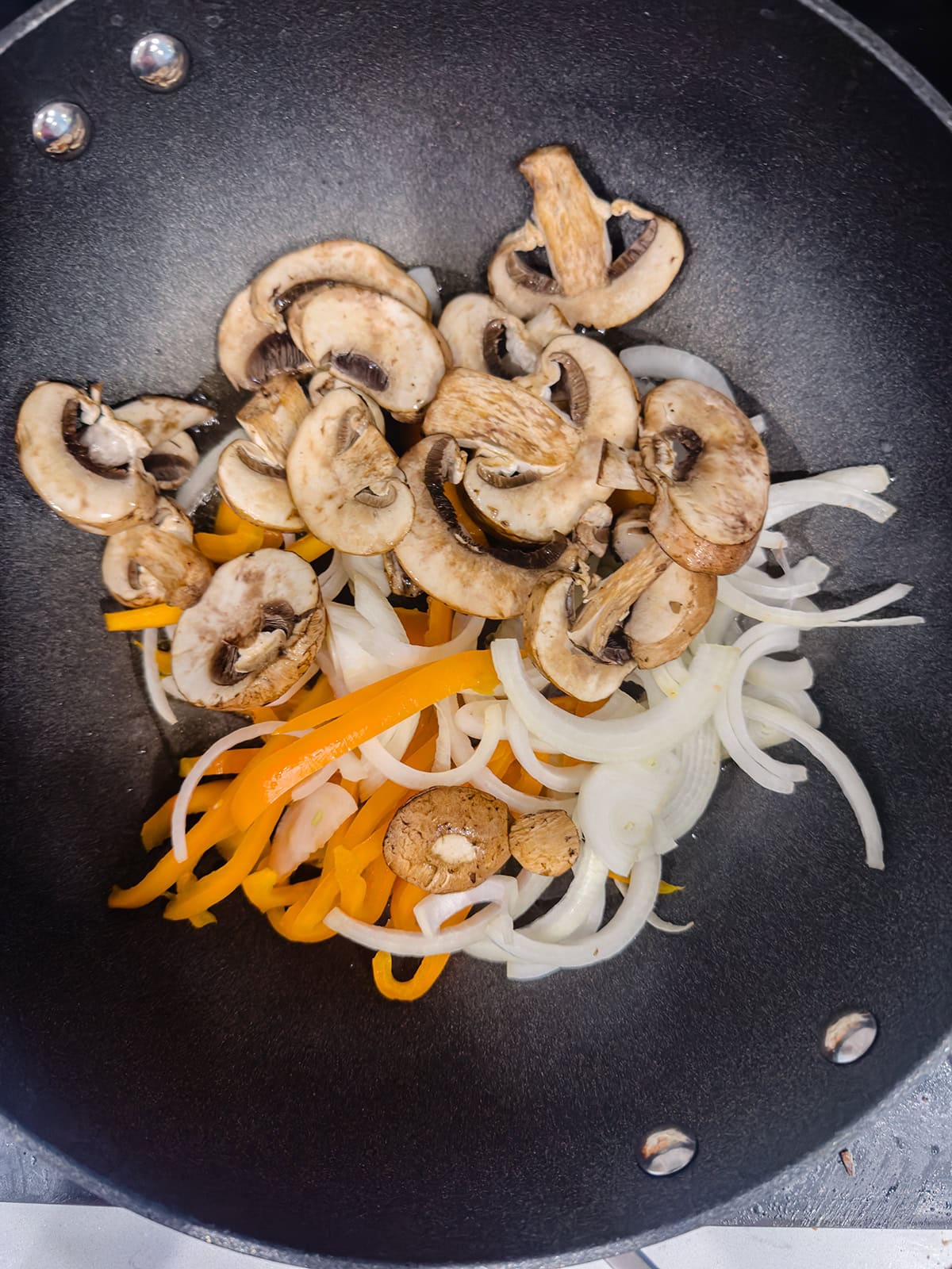 Sliced mushrooms, yellow bell peppers, and onions in a black wok, ready to be cooked for a flavorful keto chicken stir fry.