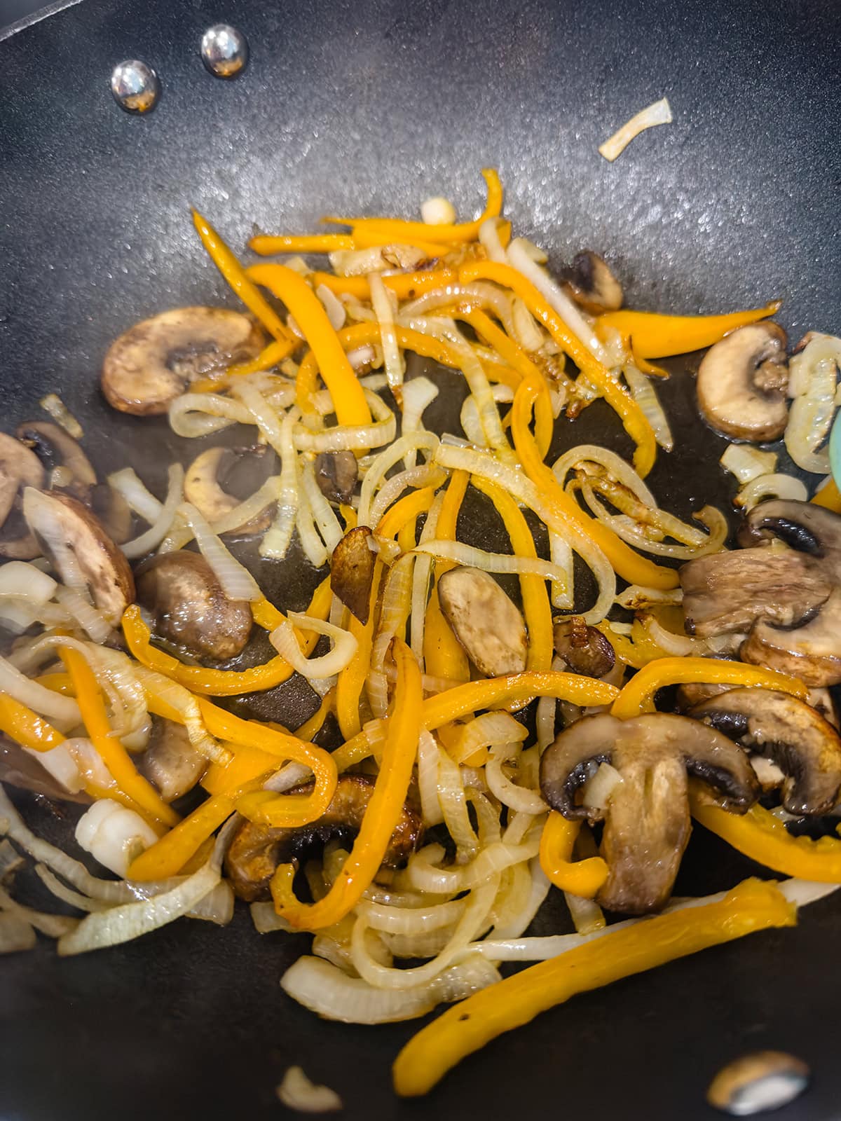 Sliced yellow bell peppers, onions, and mushrooms sautéing in a black skillet—a perfect veggie base for a keto chicken stir fry.